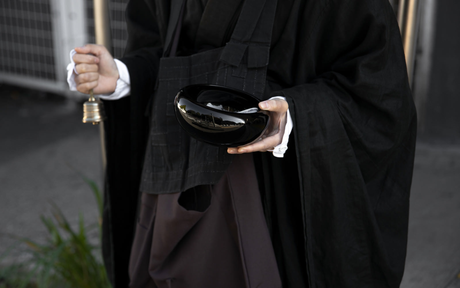 A monk in a black robe holding a begging bell and practicing alms-begging at the station plaza