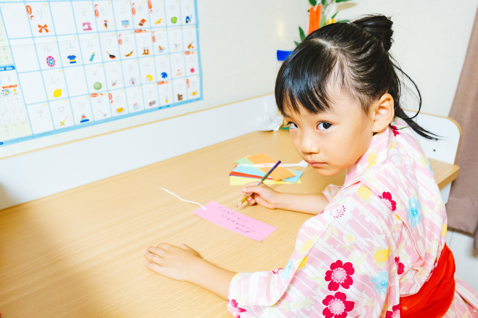浴衣を着た女の子が短冊に向かって集中している七夕の様子