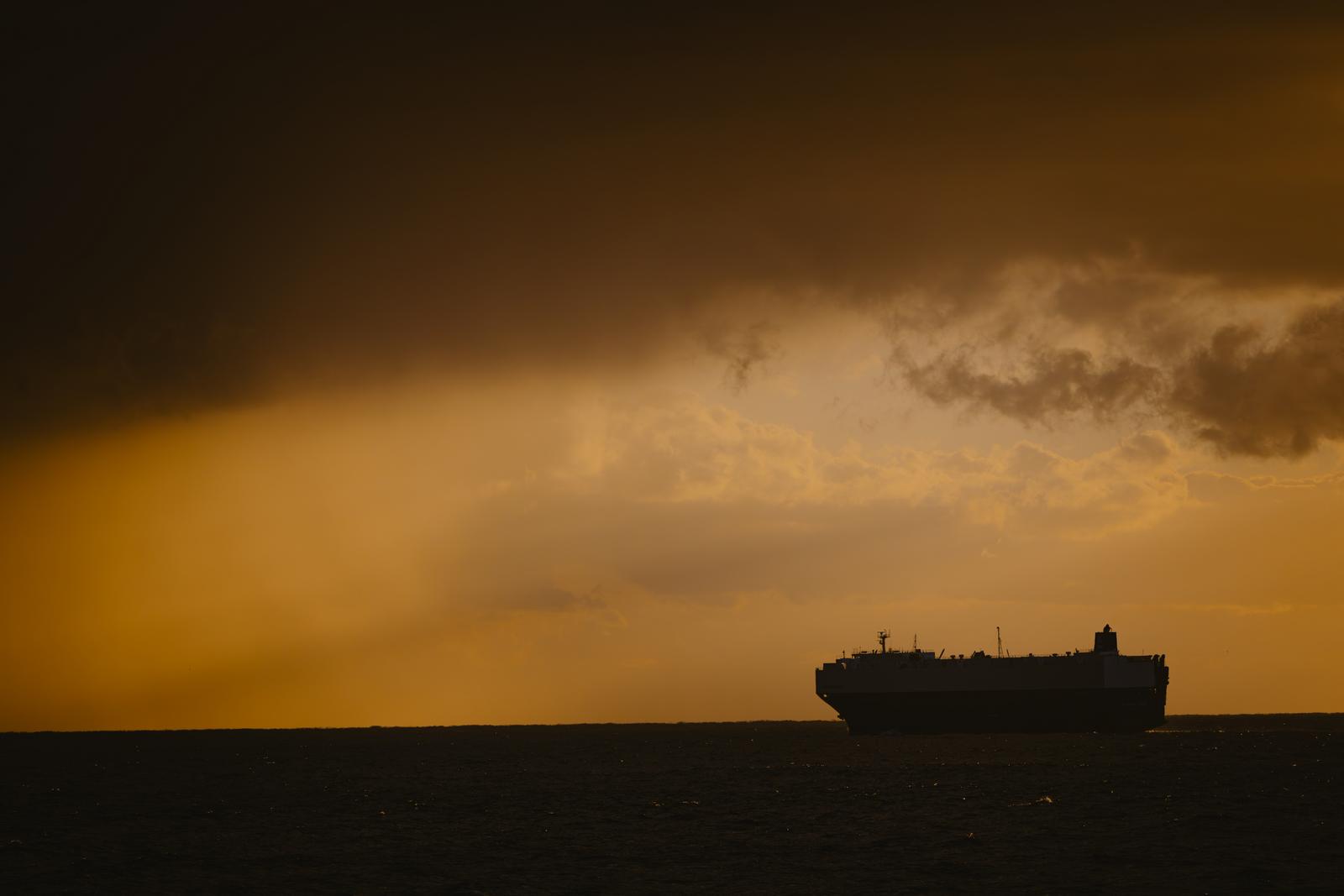 朝焼けの空の雨雲の向こうに浮かぶタンカーのシルエット