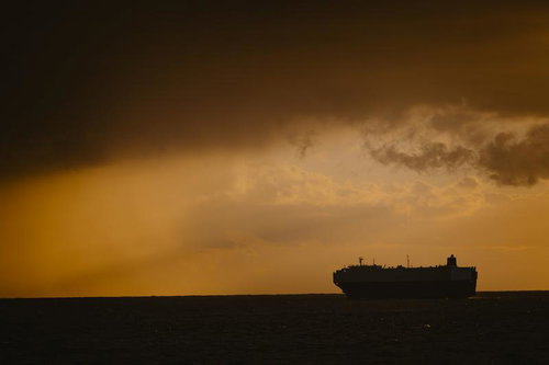 朝焼けの雨雲の向こうに浮かぶタンカーのシルエットの写真