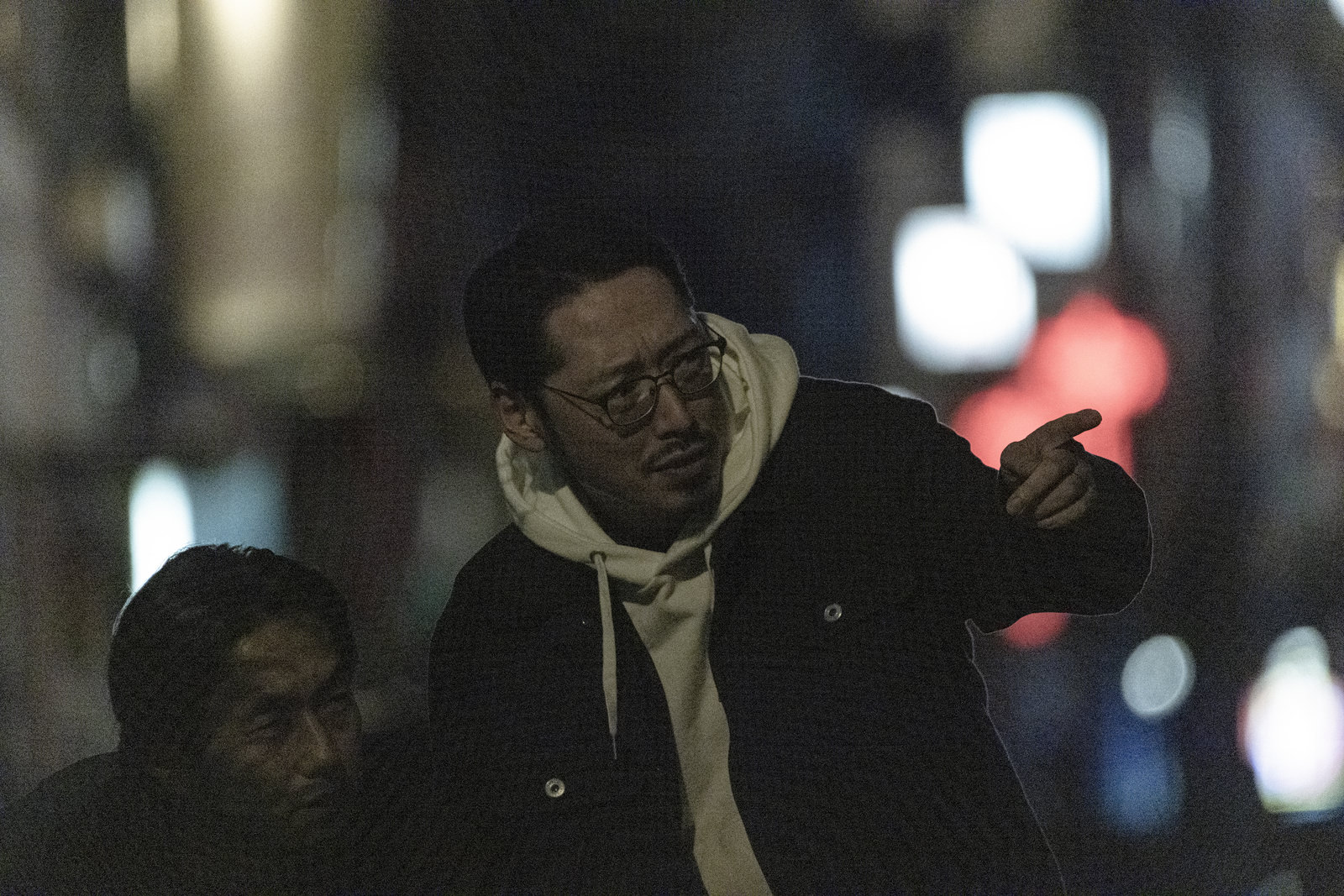 夜の街で眼鏡をかけたスーツ姿の男性が張り込みをしている探偵［モデル：ゆうせい 大川竜弥］