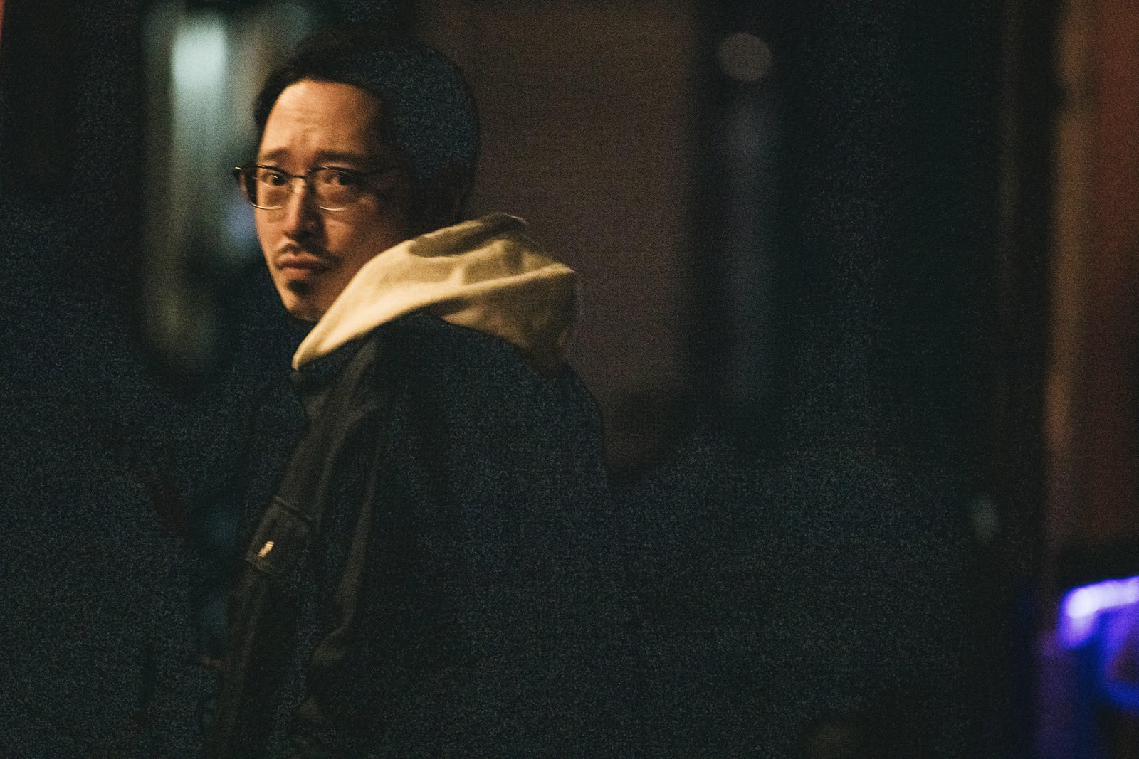 暗い場所で肩越しに振り返る男性［モデル：ゆうせい］