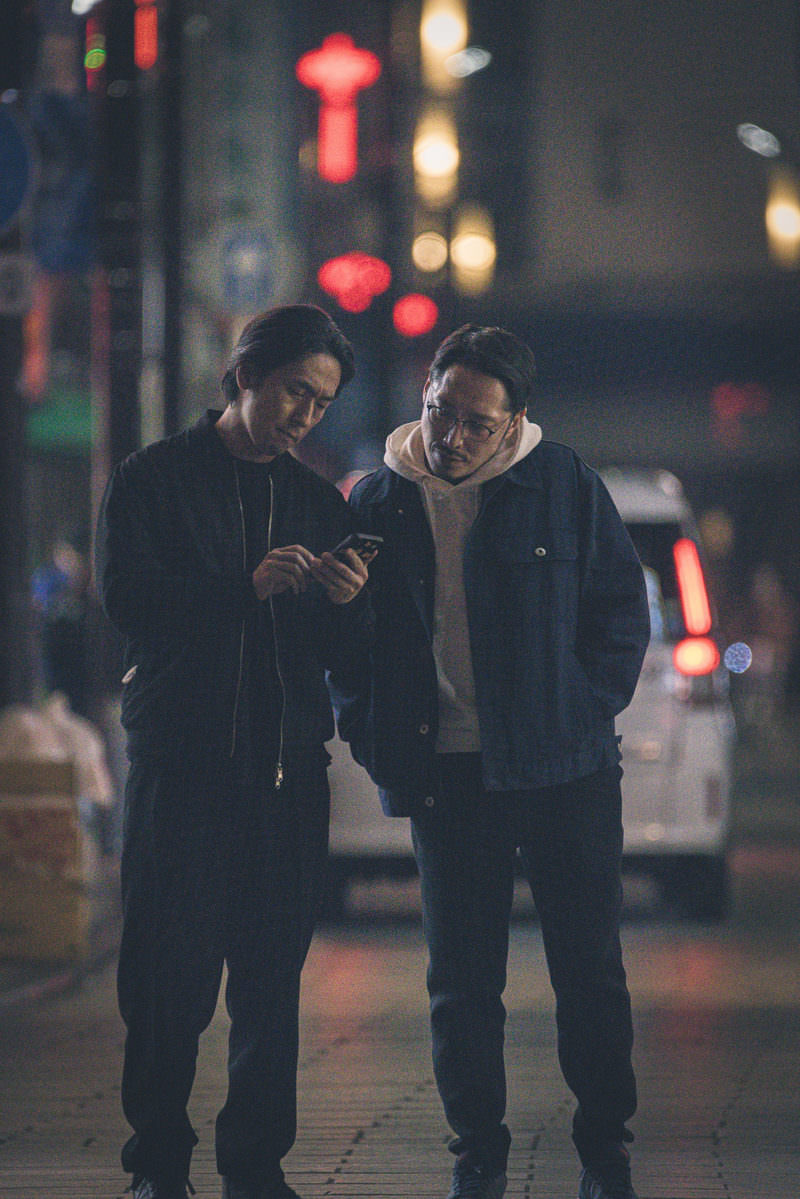 夜の繁華街でスマートフォンを見ている二人の男性［モデル：ゆうせい 大川竜弥］