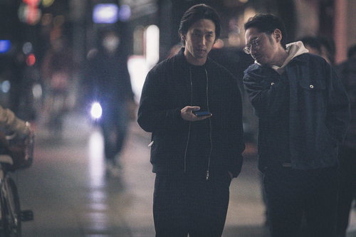 夜の繁華街で尾行対象を確認する探偵ふたり