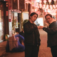 夜の繁華街で張り込み中にグータッチをするベテランラッパーの写真