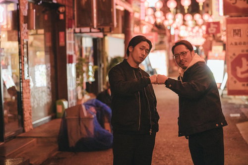 夜の繁華街で張り込み中にグータッチをするベテランラッパー