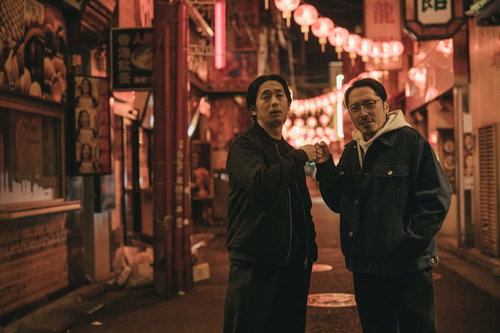 繁華街の夜間で決めるグータッチする二人の男性