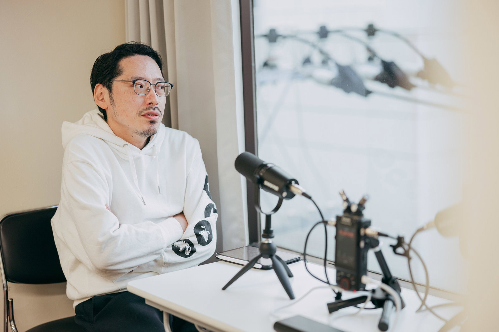 白いシャツを着た男性がマイクの前でポッドキャスト収録をしている［モデル：ゆうせい］