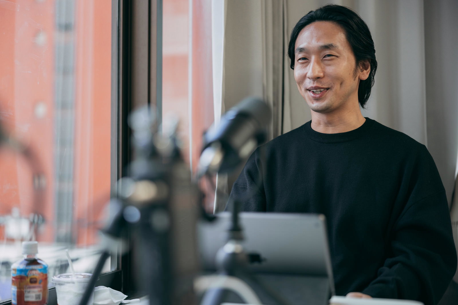 A man sitting at a desk speaking into a microphone and smiling in a studio