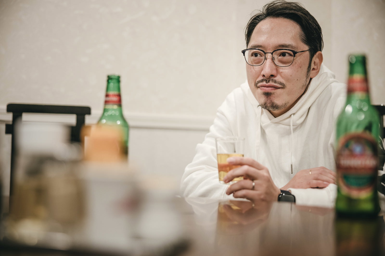 テーブルに座ってビールグラスを持ちながら待つ眼鏡をかけた男性［モデル：ゆうせい］