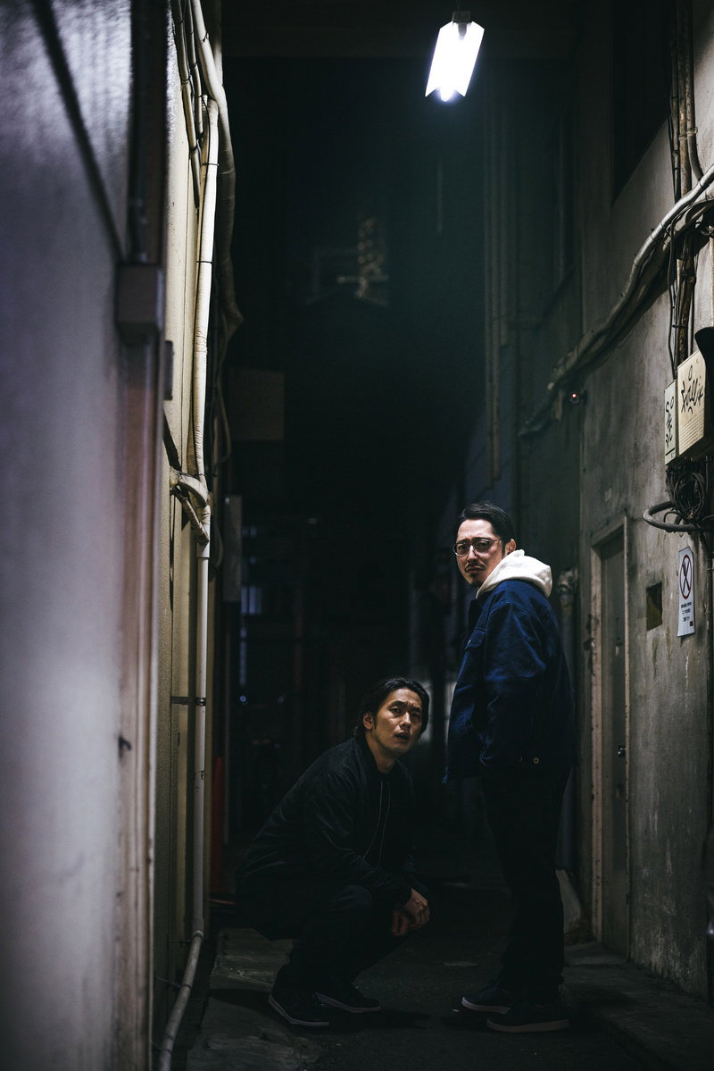 Two men hiding in a dark alley at night