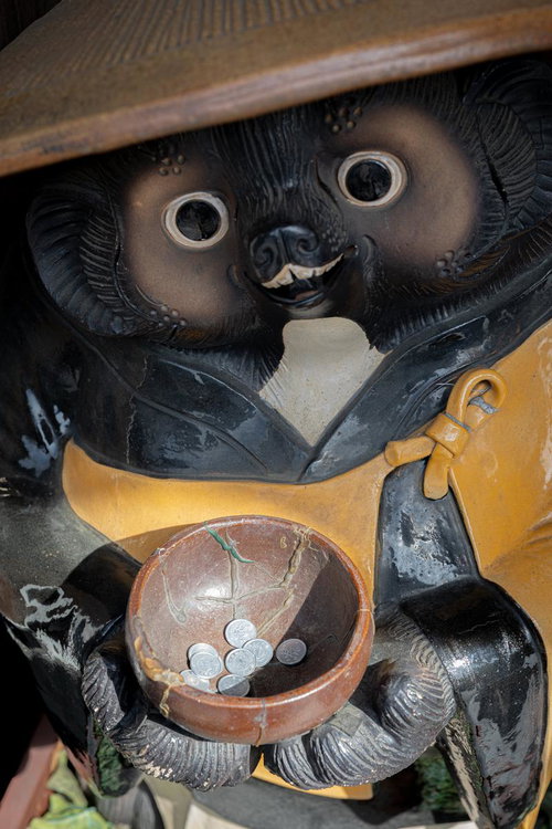 黄色い前掛けを着た狸の置物が腹に託鉢の鉢を抱える縁起物