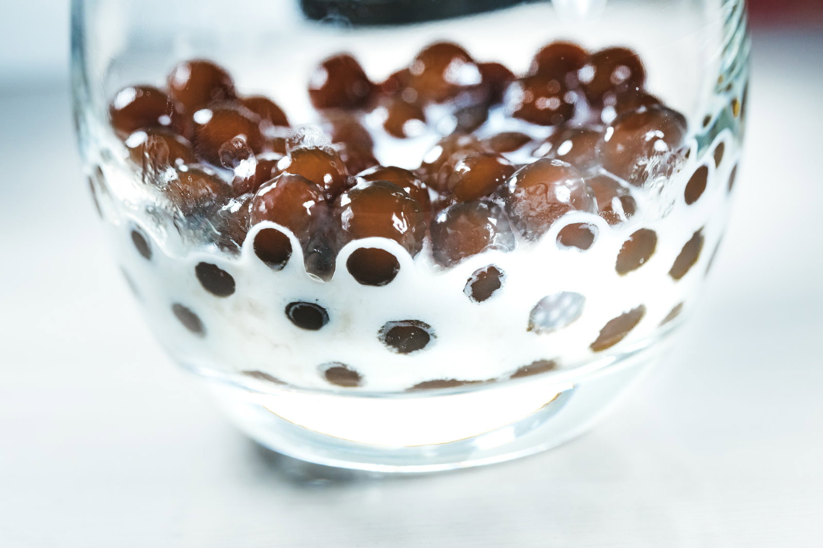 透明なグラスの底に黒いタピオカが沈殿し、上から白い牛乳が注がれている様子