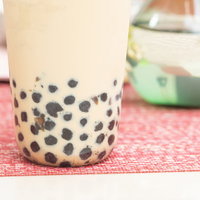 透明なグラスのミルクティーに沈殿するタピオカの写真