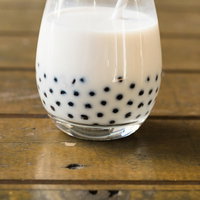 透明なグラスの底に沈殿するブラックタピオカのミルクティの写真