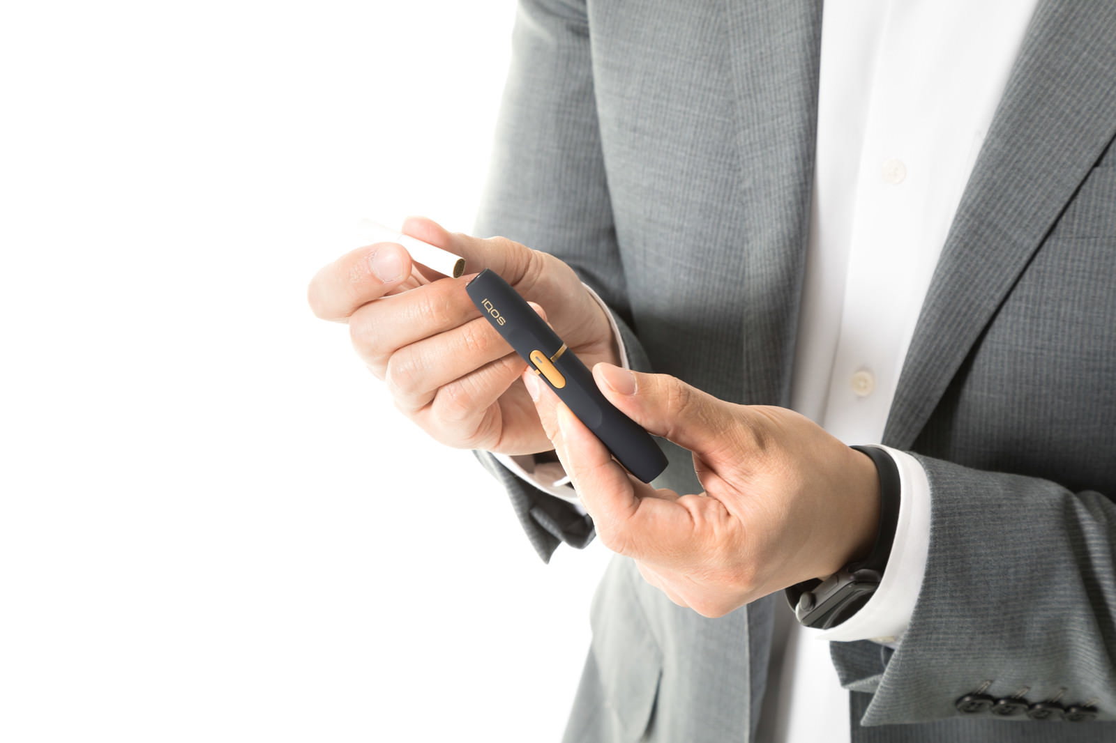 グレーのスーツを着た人がIQOSのたばこスティックをホルダーに挿入している手元［モデル：大川竜弥］