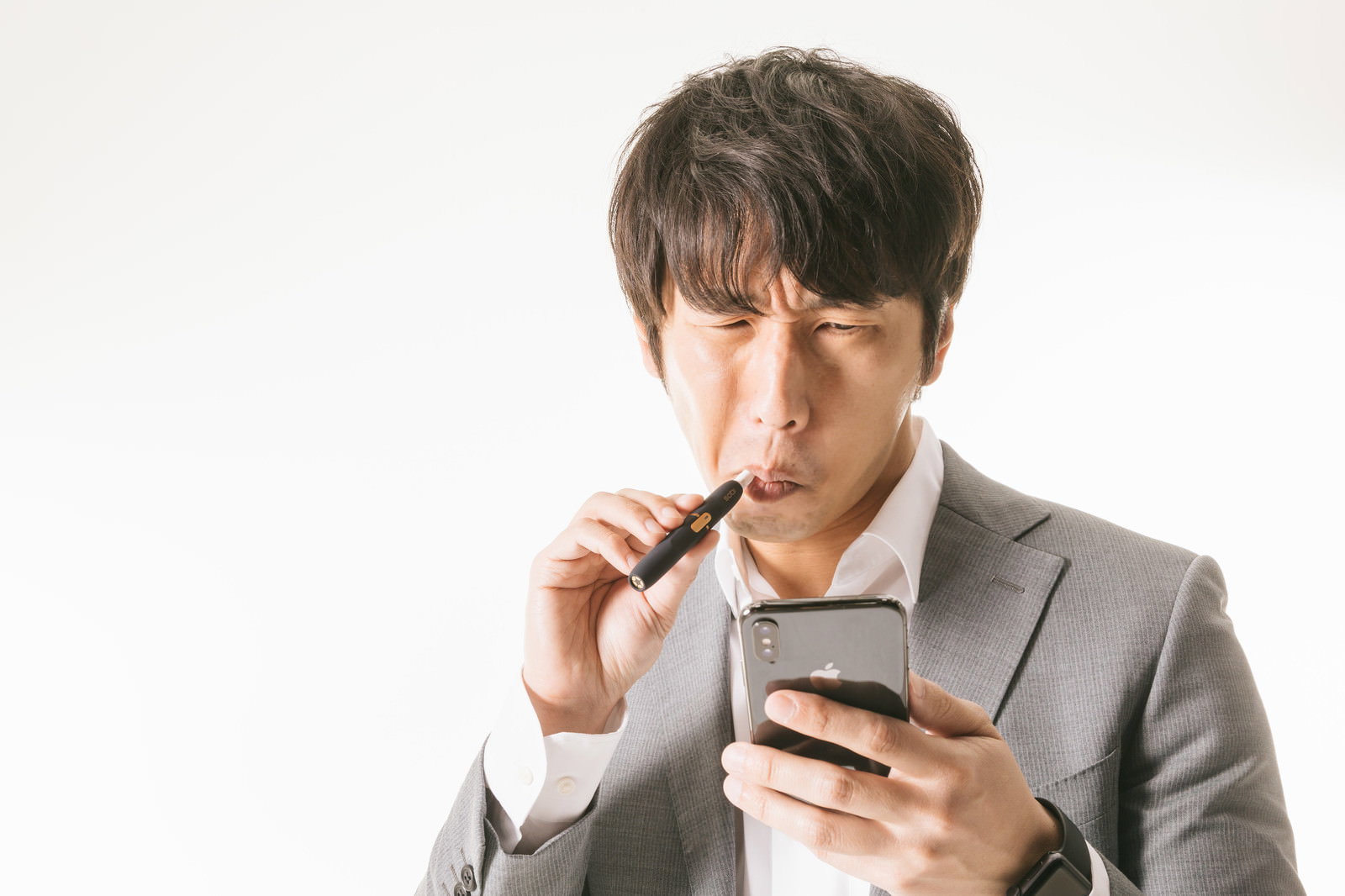電子タバコを吸いながらスマートフォンを操作するスーツ姿の男性［モデル：大川竜弥］