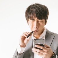 たばこ休憩中にスマートフォンで相場をチェックする投資家男性の写真