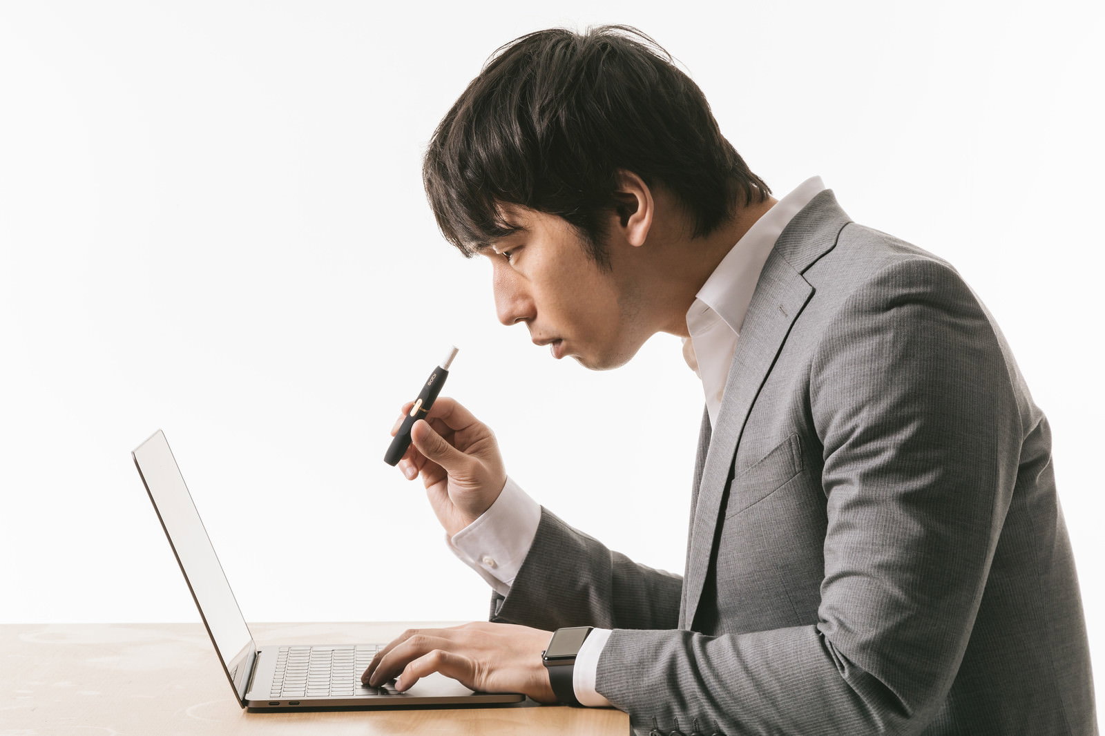 ノートパソコンの前で電子タバコを持つスーツ姿の男性［モデル：大川竜弥］