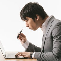 デスクワーク中にIQOSを手にするスーツ姿の男性の写真