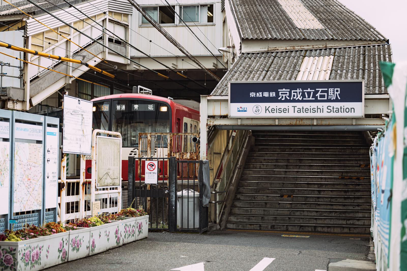 京成立石駅に停車する赤い電車と駅舎の風景