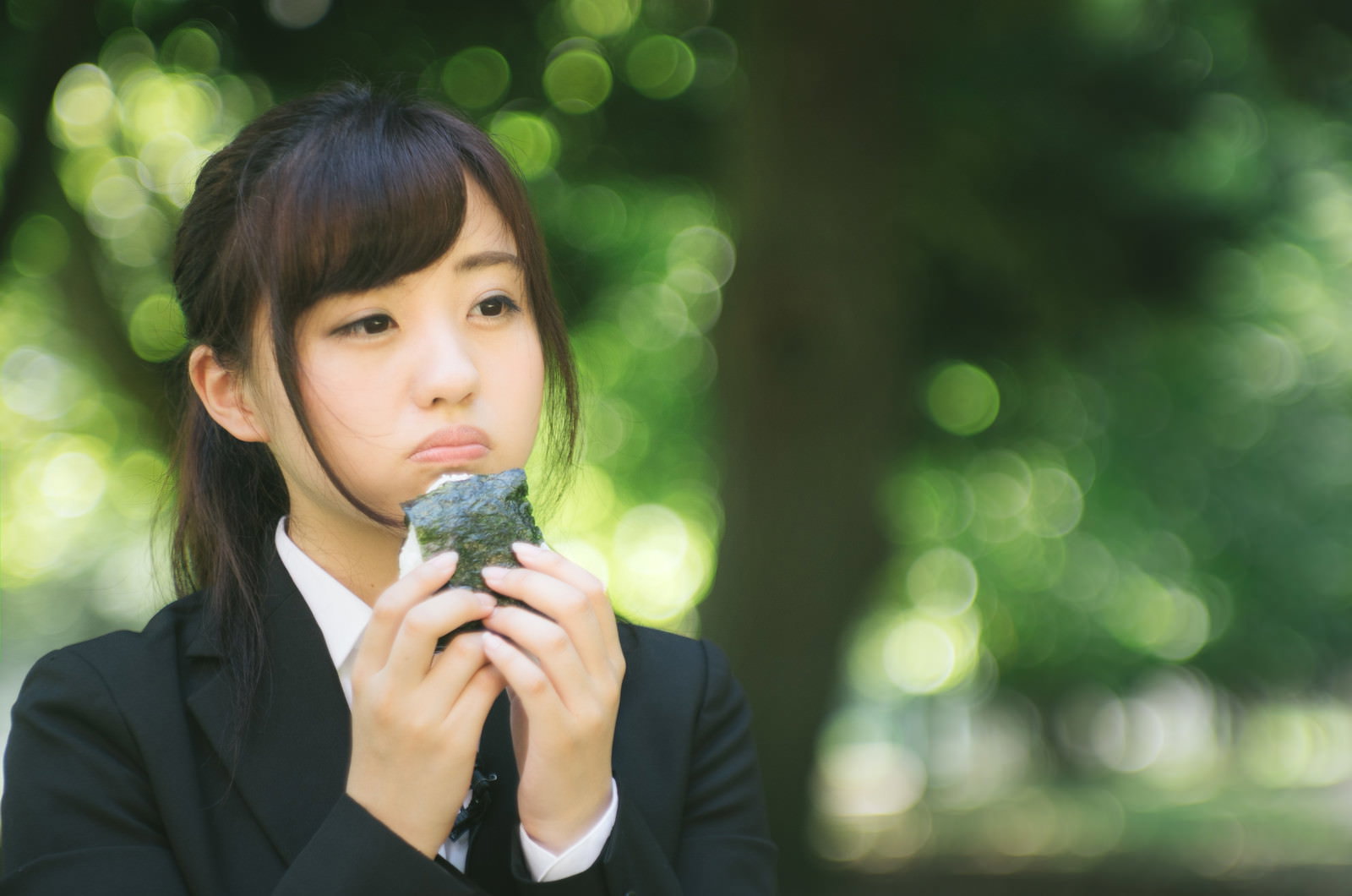 公園で一人おにぎりを食べるスーツ姿の女性［モデル：河村友歌］