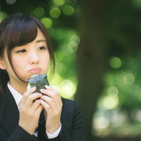 公園のベンチで孤独におにぎりを食べるスーツ姿の就活生の写真