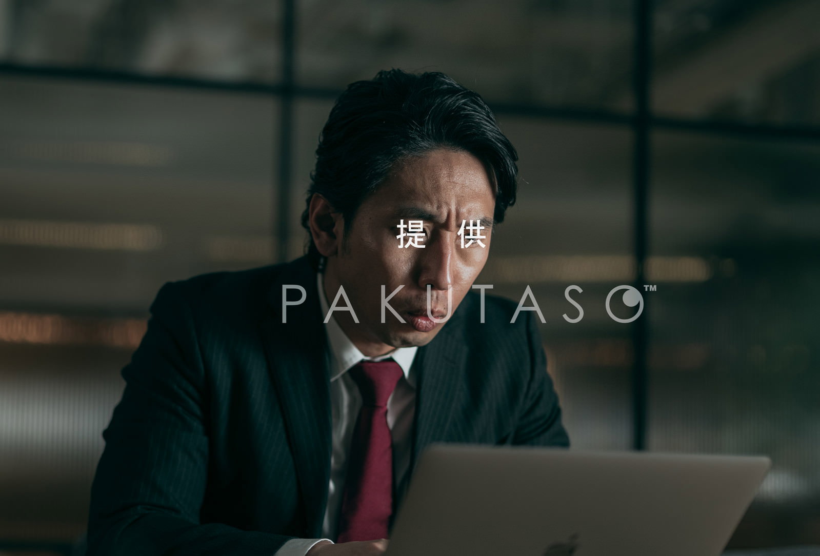 暗いオフィスでPCをにらむ険しい表情の男性［モデル：大川竜弥］
