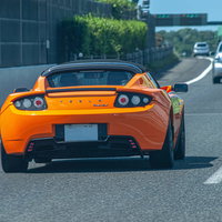 高速道路を走るオレンジ色のテスラスポーツカーの写真
