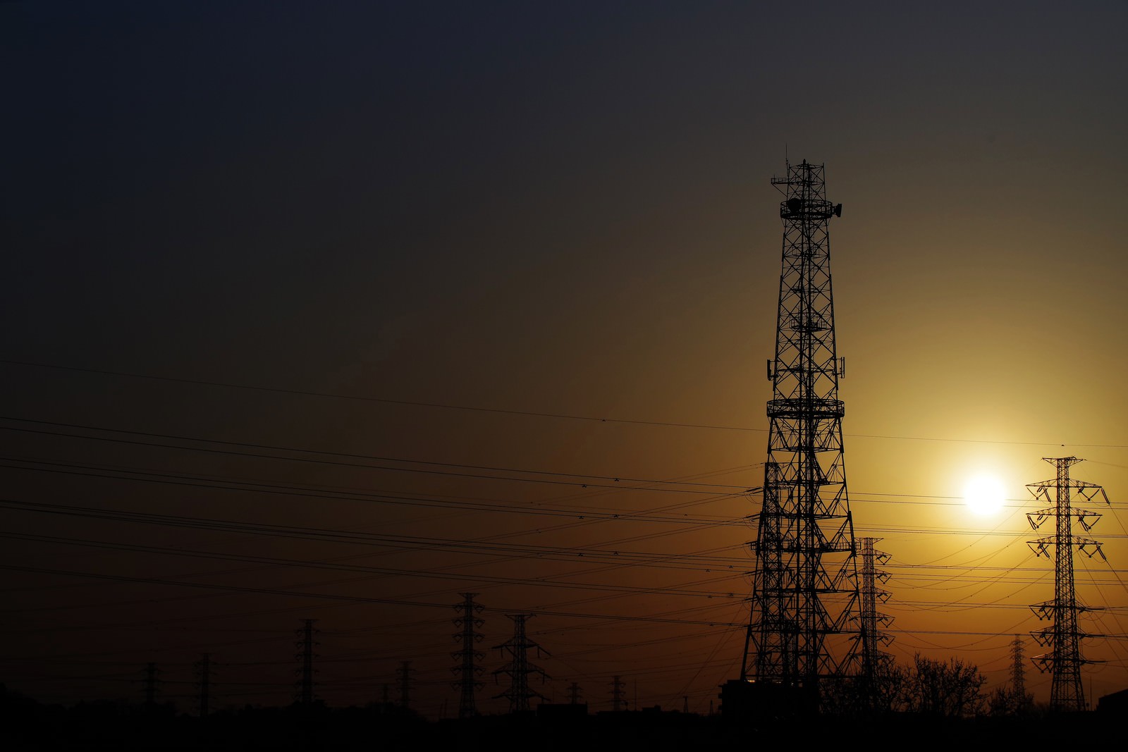 オレンジ色の夕焼け空に送電線と鉄塔のシルエットが映る風景