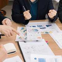 デスクの上のグラフや資料を囲んで行われるビジネス会議の写真