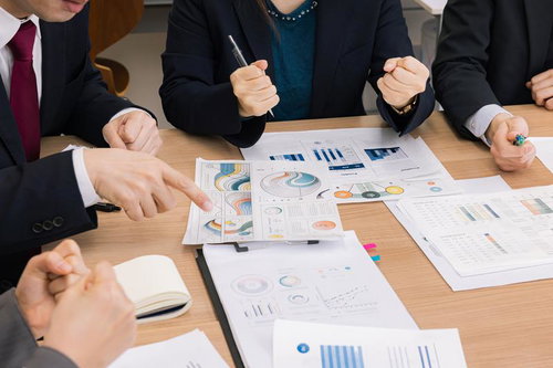 デスクの上のグラフや資料を囲んで行われるビジネス会議