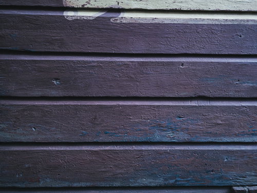 濃い紫色のペイントの跡が残る横張り外壁の板壁テクスチャー