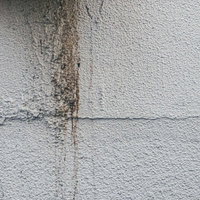 白いモルタル外壁に流れる茶色の雨ダレのシミの写真