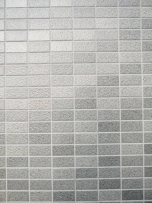 光が反射するグレーのタイル壁の建築外壁テクスチャー