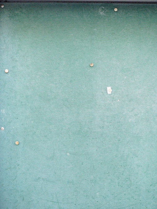 使い古された薄緑色のクロス張り掲示板に刺さった画鋲