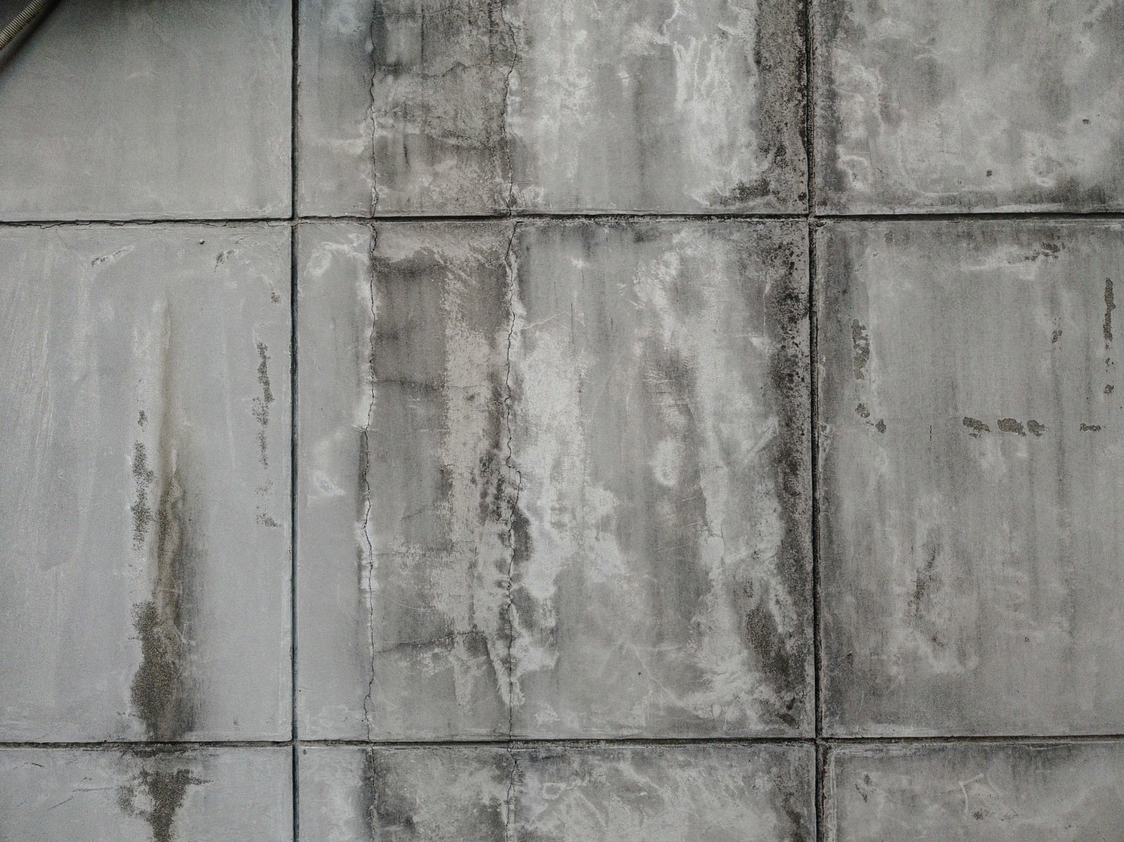ひび割れと水染みが見られるグレーのタイル壁面