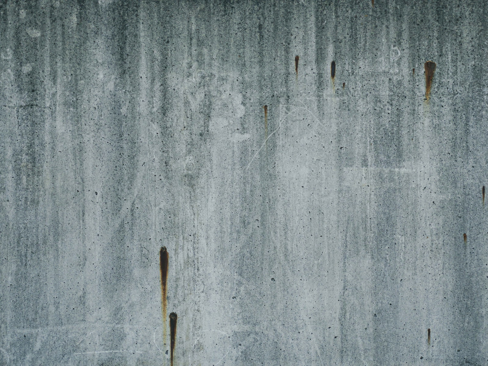 錆びた釘の跡が縦に流れるグレーのコンクリート壁