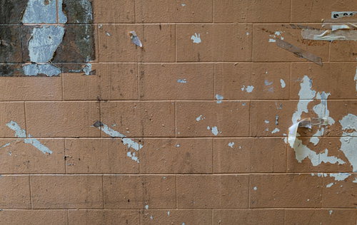 古いブロック壁に貼られたポスターの剥がれ跡と劣化テクスチャー