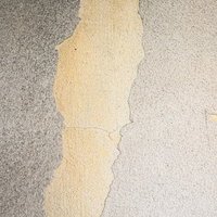 グレーのコンクリート壁に剥げ落ちる黄色い塗装の写真