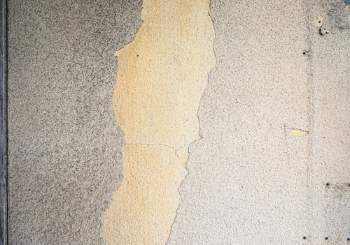 グレーのコンクリート壁に剥げ落ちる黄色い塗装