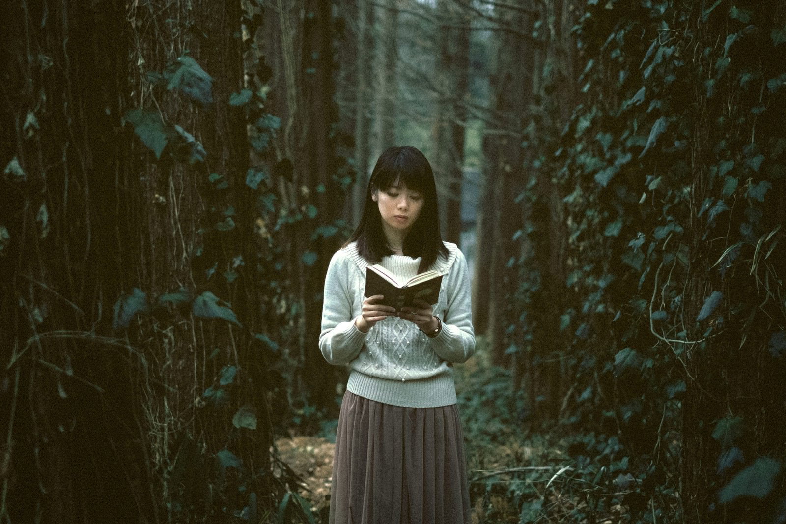 深い森の中で本を読む白いセーター姿の女性［モデル：モデルリリース］