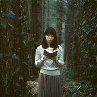 深い森で本を読む白いセーター姿の長黒髪女性の写真