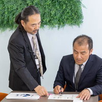 印刷した資料を見ながら指摘する男性社員の打ち合わせシーンの写真