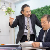 ホワイト企業の打ち合わせで資料を前に説明する役員と男性社員の写真