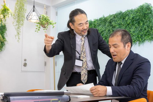 ホワイト企業の打ち合わせで資料を前に説明する役員と男性社員