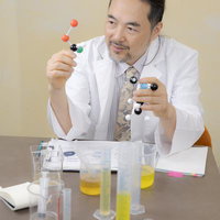 分子モデルを持って説明する白衣の男性研究者の写真