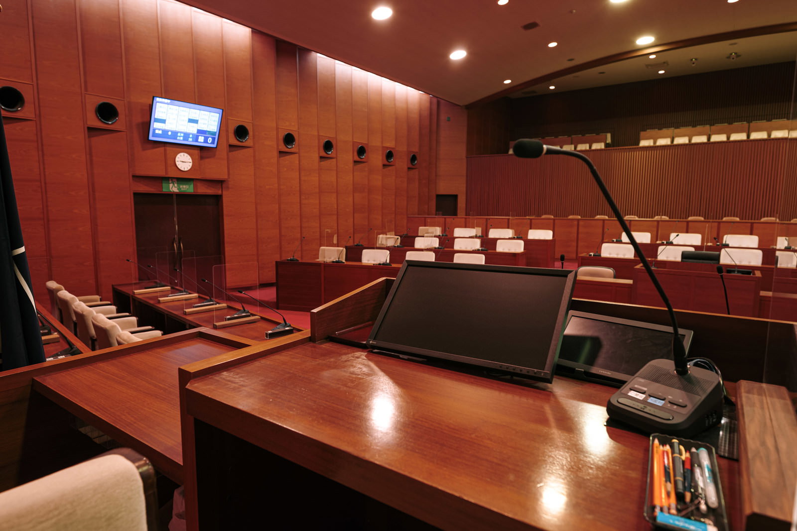 赤茶色の議場内に電子表決モニターと議員席が見える津山市議会の議場
