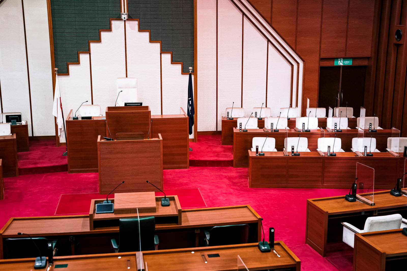 赤いカーペットの議場で市議会議員が座る木製の議員席が段状に配置されている