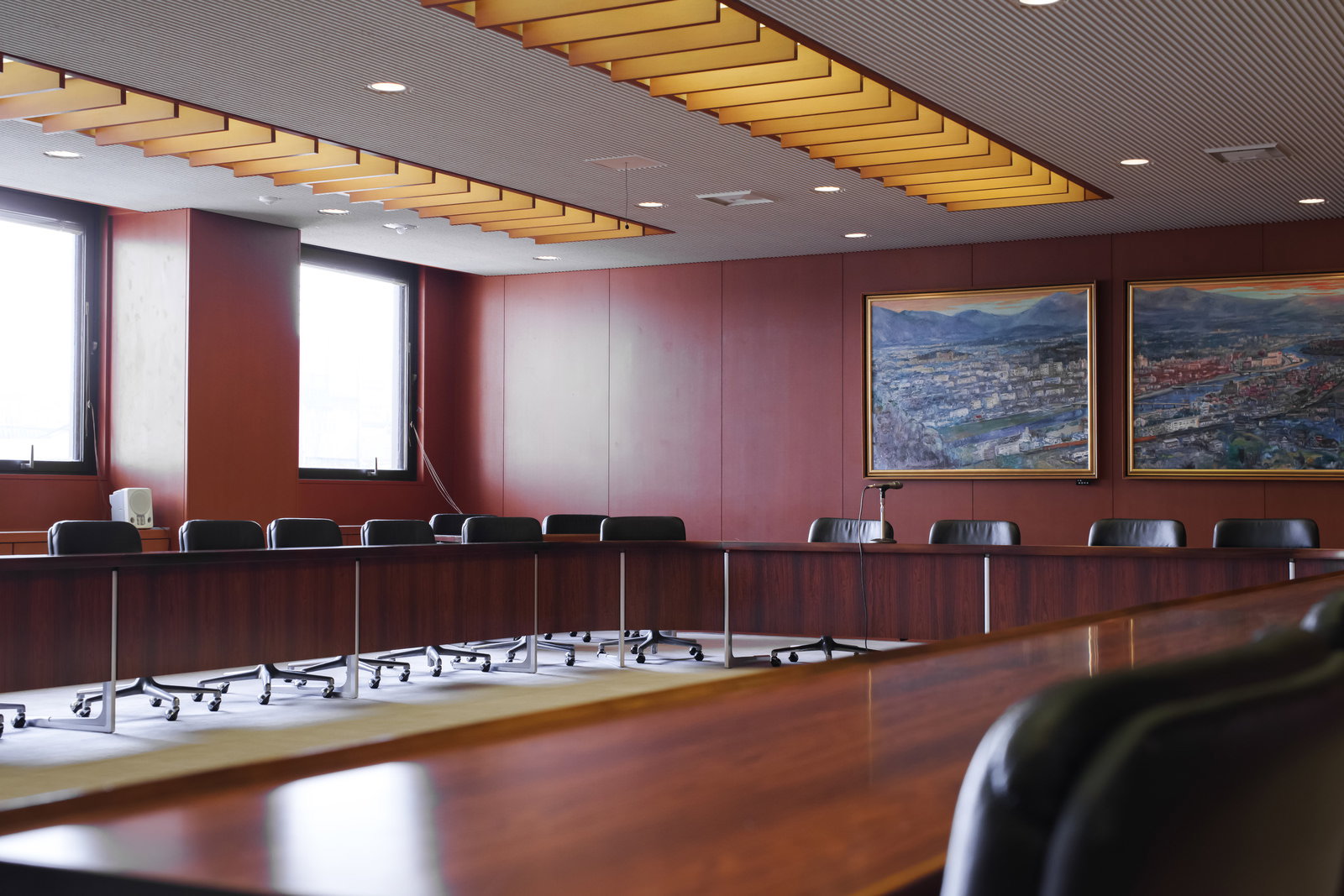 赤紫色の壁と黄色い天井梁のある広い協議会室で、木製テーブルと黒い椅子が並んでいる